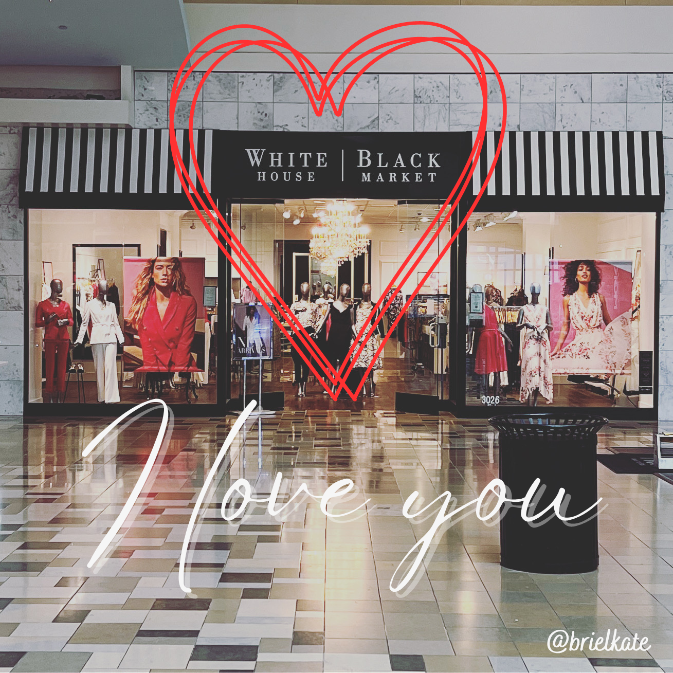 Picture of a White House Black Market (WHBM) boutique inside of a shopping mall. The WHBM logo is surrounded by the outline of a red heart, with the text "I love you" written in white text below the heart.