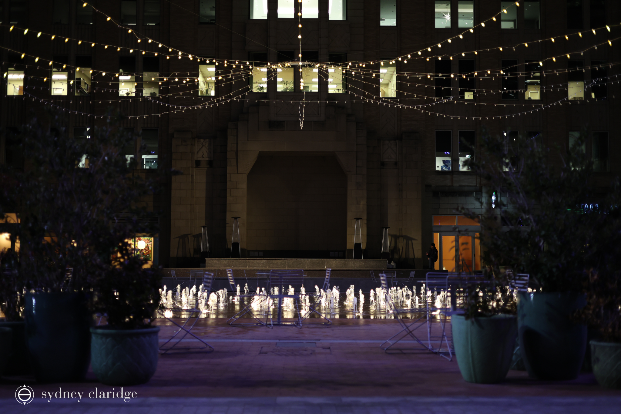 Sundance Square Plaza with string lights over the plaza, and fountains lit. There is an outdoor stage in the background.